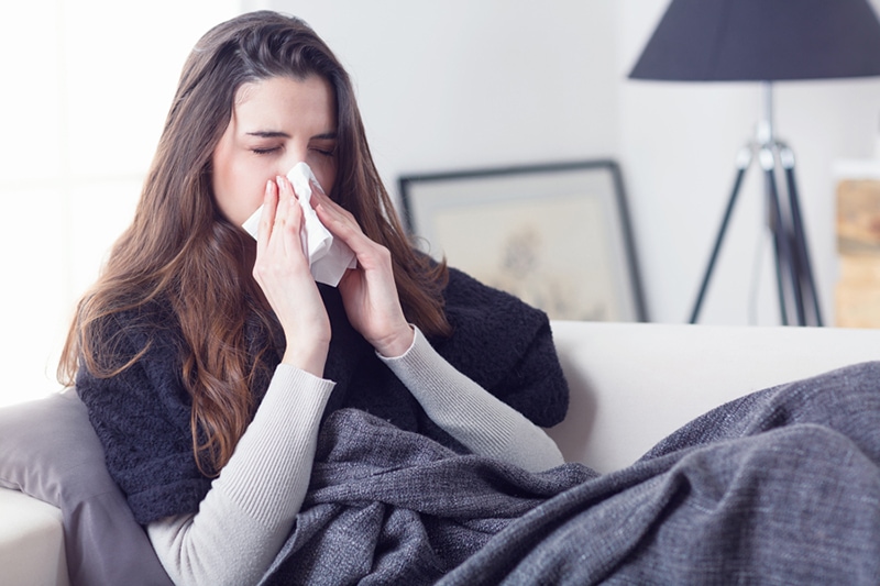 Blog Title: What Does Indoor Air Quality Have to Do With Allergies? Photo: woman sneezing into tissue