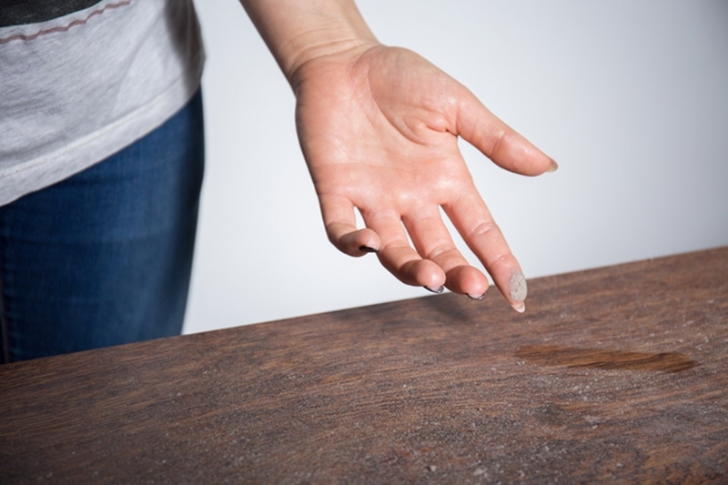 Close-up of dust on woman finger taken from wooden table in Austin