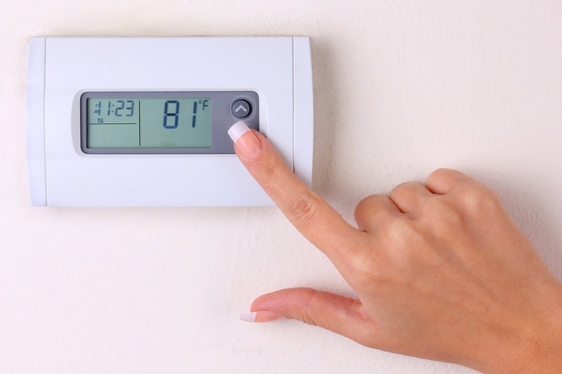 Thermostat 101 Basics. Photo of a person pressing a button on a thermostat mounted on a wall.