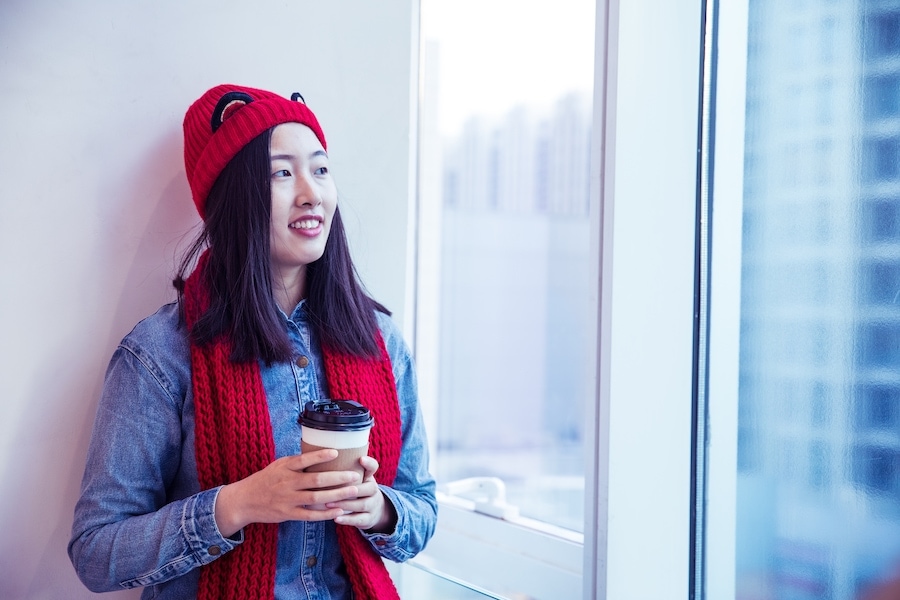 Young woman holding coffee by window.