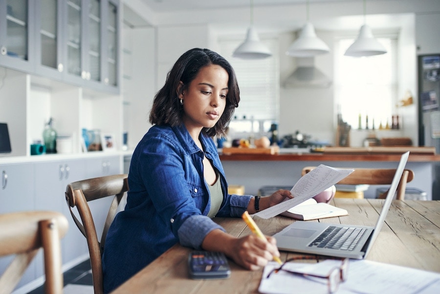 Shot of a young woman using a laptop and going through paperwork while working from home.